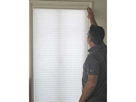 A man wearing a polo shirt installing shades on a tall window